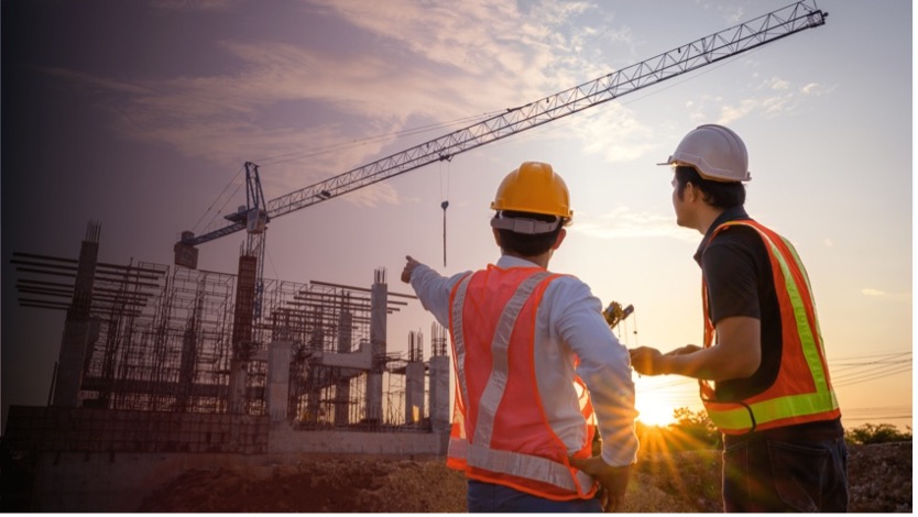 Two construction managers in safety gear overseeing a large building site with a crane at sunset, representing the future of luxury construction in Marbella.